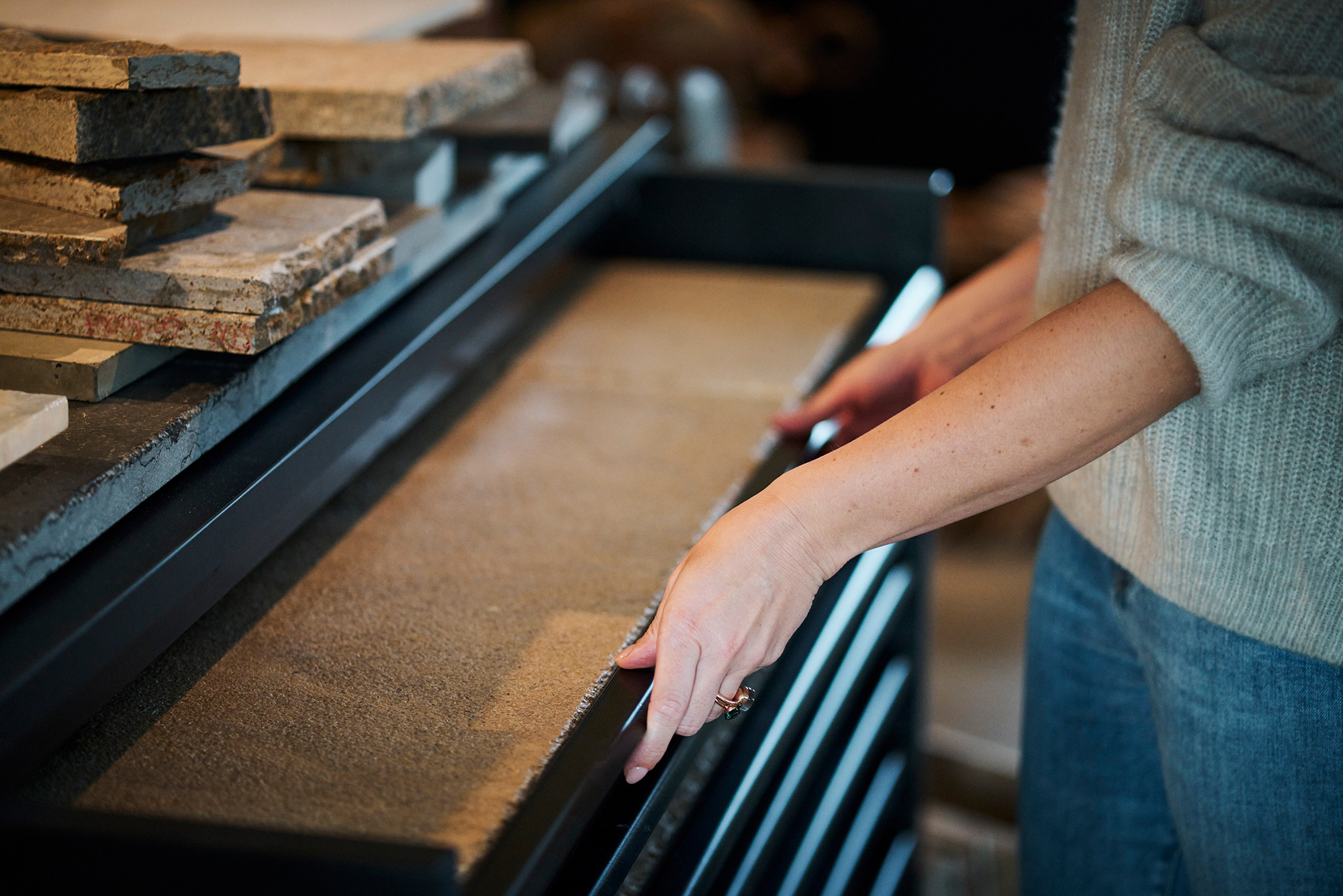 Bild von einer Dame vor eine Schwarzen Anrichte. Die oberste Schublade ist geöffnet. In der Schublade sind Baumaterialien, ebenso auf der Anrichte. Die Frau trägt eine blaue Jeans und einen hellen Pullover.